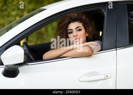 Belle jeune femme arabe à l'intérieur d'une belle voiture blanche en regardant par la fenêtre. Fille arabe portant des vêtements décontractés. Banque D'Images