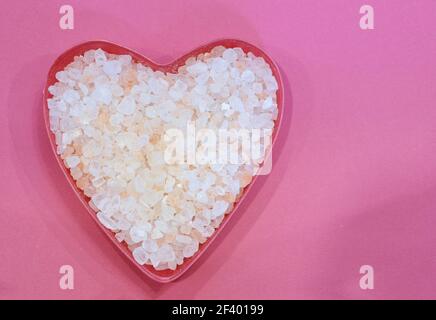 Sel de l'Himalaya en forme de coeur sur fond rose, vue de dessus. Cristaux de sel rose. Concept d'alimentation saine Banque D'Images