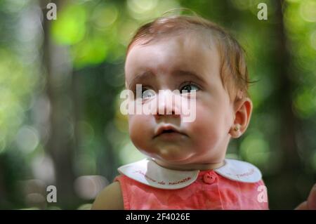 Bébé fille de six mois s'amusant dehors. Portrait en gros plan de bébé fille de six mois regardant quelque chose à l'extérieur avec un arrière-plan défoqué. Banque D'Images