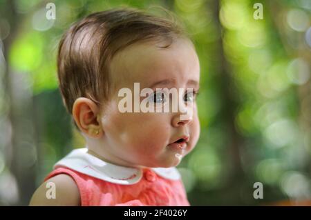 Bébé fille de six mois s'amusant dehors. Portrait en gros plan de bébé fille de six mois regardant quelque chose à l'extérieur avec un arrière-plan défoqué. Banque D'Images