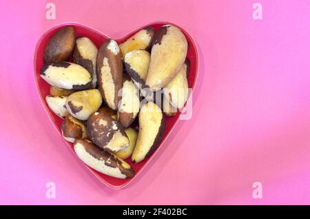 Noix brésiliennes en forme de coeur sur fond rose, vue de dessus. Aliments sains noix du brésil, concept de produit végétalien Banque D'Images