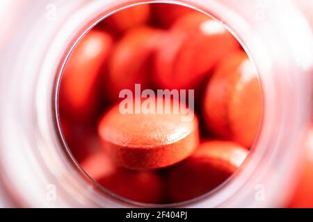 Vue d'en haut en profondeur dans un petit pot en verre ou en plastique rempli de pilules rouges et de comprimés. Concentrez-vous sur la tablette rouge supérieure. Faible profondeur de champ Banque D'Images