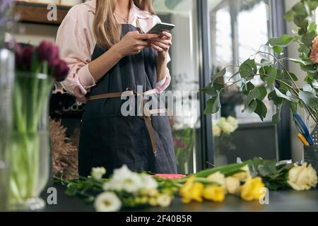 Photo du fleuriste tenant le téléphone et faisant la photo de belles fleurs couchée sur la table dans la boutique de fleurs, l'espace de copie. Boutique de fleurs Lifestyle. Magnifique Banque D'Images
