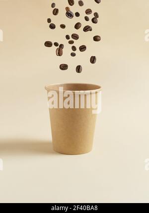 Les grains de café volent dans une tasse de papier sur fond jaune. Concept de nourriture volante. Copier l'espace. Banque D'Images