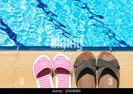 Une paire de sandales pour hommes et femme à côte de la piscine Banque D'Images