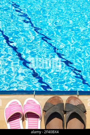 Une paire de sandales pour hommes et femme à côte de la piscine Banque D'Images