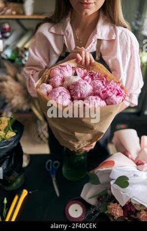 Image en gros plan d'une fleuriste féminine qui fait un beau bouquet de fleurs fraîches. Portrait d'un fleuriste moderne couronné de succès portant un tablier Banque D'Images