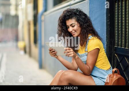 Jeune femme arabe à digital tablet outdoors. African girl wearing vêtements décontractés fond inurban. Curly hairstyle. Banque D'Images