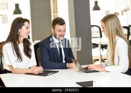 Femme blonde agent d'assurance ou de conseiller en placement expliquant avec ordinateur portable à un jeune couple. Banque D'Images