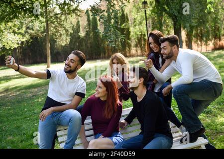 Groupe d'amis prenant en selfies parc urbain. Cinq jeunes gens portant des vêtements décontractés. Banque D'Images