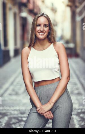 Young woman smiling en contexte urbain. Fille blonde avec tout droit de porter les tenues de coiffure dans la rue. Banque D'Images