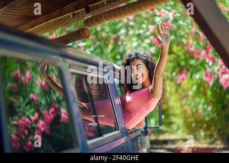 Fille souriante dans une camionnette de camping appréciant le printemps dans un beau camping aux fleurs roses. Femme arabe qui se lève par la fenêtre d'une camionnette. Une fille arabe heureuse qui se lève par la fenêtre d'une fourgonnette Banque D'Images