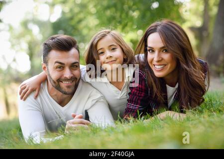 Une bonne famille dans un parc urbain. Père, mère et petite fille qui pond sur l'herbe. Une bonne famille dans un parc urbain Banque D'Images