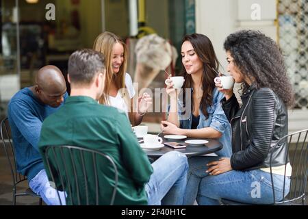 Groupe multiracial de cinq amis en buvant un café ensemble. Trois femmes et deux hommes au café, parler, rire et profiter de leur temps. Les concepts de vie et de l'amitié avec des personnes réelles maquettes Banque D'Images