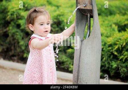 Adorable petite fille qui boit de l'eau dans une fontaine du parc. Une petite fille boit de l'eau dans une fontaine du parc Banque D'Images