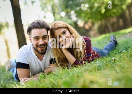 Beau jeune couple allongé sur l'herbe dans un parc urbain. Homme et femme caucasiens portant des vêtements décontractés. Blonde femme. Beau jeune couple allongé sur l'herbe dans un parc urbain. Banque D'Images