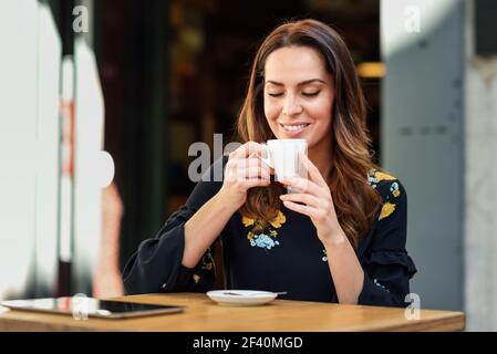 Une jeune femme boit du café dans un café-bar urbain. Femme d'âge moyen assise à une table sur une terrasse extérieure. Fille avec la californie met en vedette la coiffure.. Femme d'âge moyen qui boit du café dans un café-bar urbain. Banque D'Images