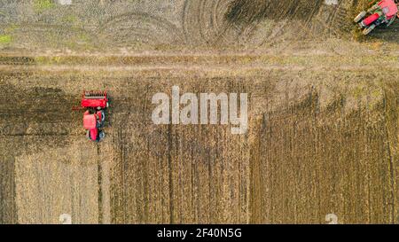 Vue aérienne de dessus de trois tracteurs, l'un traînant une herse à disque et l'autre un cultivateur de semis, le troisième tirant la machine de semoir sur le fie arable Banque D'Images