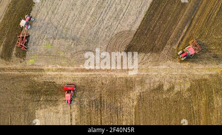 Vue aérienne de dessus de trois tracteurs, l'un traînant une herse à disque et l'autre un cultivateur de semis, le troisième tirant la machine de semoir sur le fie arable Banque D'Images