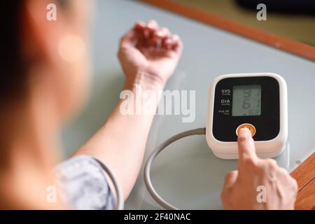 Femme avec mesure de la basse pression sanguine avec un appareil de mesure électronique à la maison. Femme mesurant sa propre tension artérielle à la maison. Banque D'Images