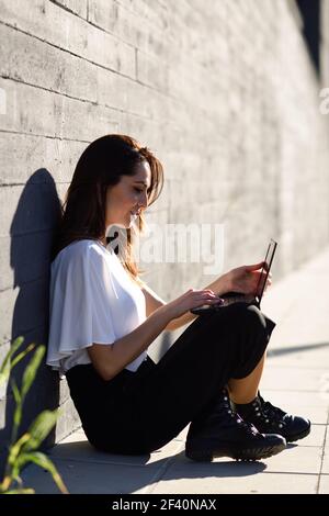 Femme d'affaires d'âge moyen travaillant avec son ordinateur portable assis sur le sol à l'extérieur. Jeune femme d'affaires travaillant avec son ordinateur portable assis sur le sol. Banque D'Images
