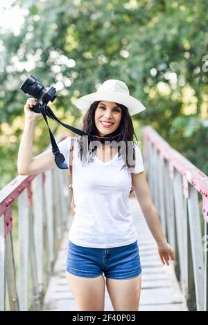 Belle jeune femme randonneur prenant des photos avec un appareil photo sans miroir, portant un chapeau de paille, randonnée dans la campagne. Une randonneur prend des photos avec un appareil photo sans miroir Banque D'Images