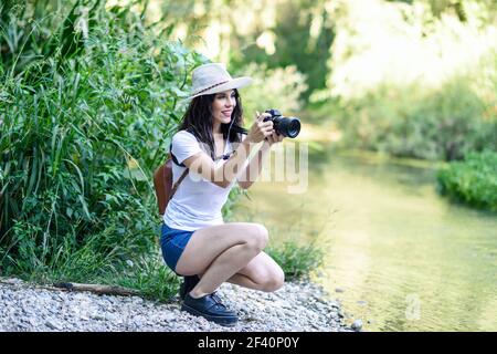 Belle jeune femme randonneur prenant des photos avec un appareil photo sans miroir, portant un chapeau de paille, randonnée dans la campagne. Une randonneur prend des photos avec un appareil photo sans miroir Banque D'Images