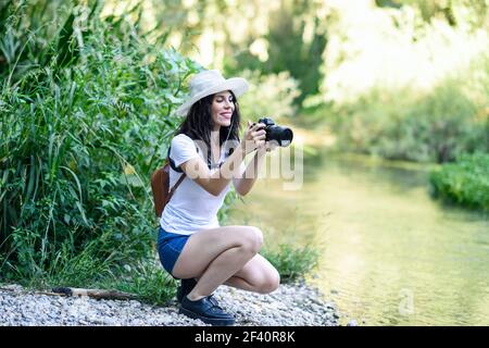 Belle jeune femme randonneur prenant des photos avec un appareil photo sans miroir, portant un chapeau de paille, randonnée dans la campagne. Une randonneur prend des photos avec un appareil photo sans miroir Banque D'Images