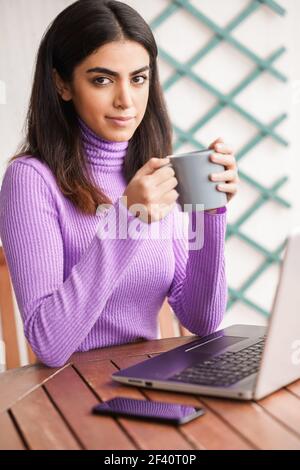 Femme persane assise dans un fauteuil sur son balcon à l'aide d'un ordinateur portable. Femme persane sur son balcon en utilisant un ordinateur portable Banque D'Images