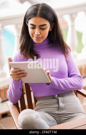 Femme persane assise dans un fauteuil sur son balcon à l'aide d'une tablette numérique. Femme persane sur son balcon utilisant une tablette numérique Banque D'Images