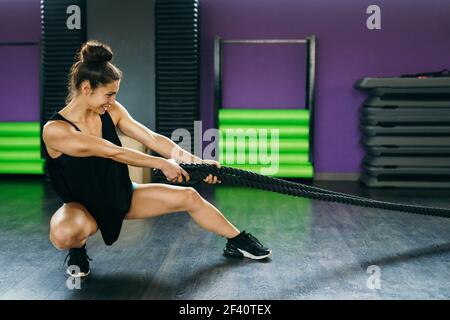 Jeune femme sportive utilisant des cordes d'entraînement dans une salle de gym. Concept de fitness.. Jeune femme sportive utilisant des cordes d'entraînement dans une salle de gym. Banque D'Images