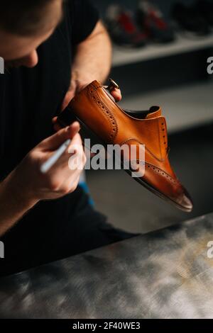Vue de dessus du cordonnier peignant le talon et la semelle de chaussures en cuir brun clair avec brosse pendant les travaux de restauration. Banque D'Images