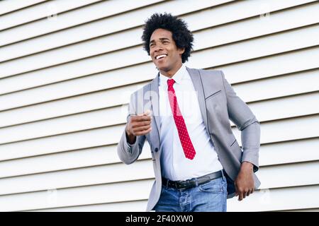 Joyeux homme d'affaires noir vêtu d'un costume dansant à l'extérieur. Homme avec cheveux afro.. Joyeux homme d'affaires noir vêtu d'un costume dansant à l'extérieur. Banque D'Images