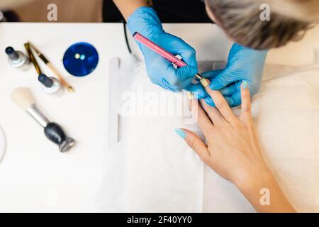 Gros plan de la Beauticienne peignant ses ongles de client et de rsquo en vernis à ongles bleu et jaune dans un centre de beauté. Gros plan de la Beauticienne peignant ses ongles de client et de rsquo en vernis à ongles bleu et jaune. Banque D'Images