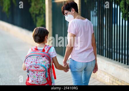 Fille de neuf ans avec sac marchant avec sa mère main dans la main portant des masques. Concept de retour à l'école. Fille de neuf ans avec sac marchant avec sa mère main dans la main. Banque D'Images