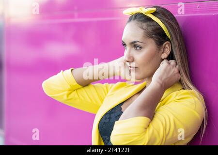 Jeune femme portant une veste et un bandeau jaunes, près d'un mur violet urbain. Jeune femme portant une veste et un bandeau jaunes Banque D'Images