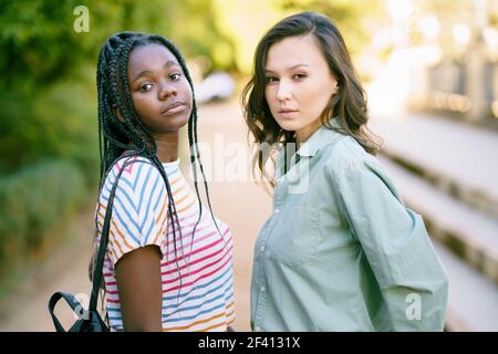 Deux jeunes amis regardant ensemble l'appareil photo dans la rue. Femmes multiethniques.. Deux femmes multiethniques regardant ensemble la caméra dans la rue. Banque D'Images