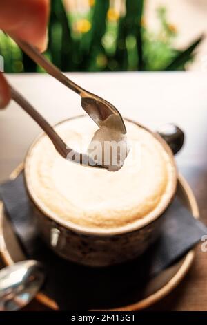 Ajoutez du sucre dans une tasse de café latte chaud sur une table en bois image couleur vintage. Ajouter le sucre dans la tasse de café latte chaud sur une table en bois Banque D'Images