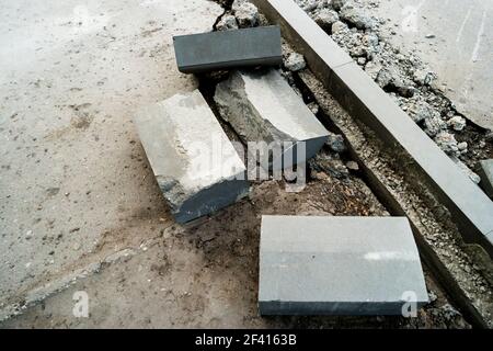 Des tas de pierres à bordure couchés sur le trottoir près de la fosse pour l'installation d'une bordure. Surface d'asphalte cassée de l'autre côté. Un trou dans la surface de la route. Réparation de travaux routiers. Des tas de pierres à bordure couchés sur le trottoir près de la fosse pour l'installation d'une bordure. Surface d'asphalte cassée de l'autre côté. Réparation de travaux routiers Banque D'Images