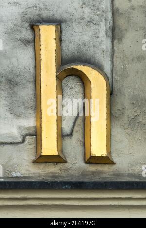 Lettre d'or historique h avec serifs sur un mur gris Banque D'Images