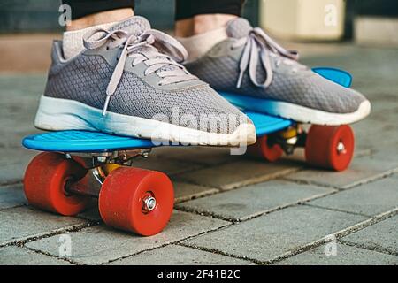 Photo d'une fille et d'un rsquo portant de vieilles sneakers qui se tient sur un skateboard bleu sur un trottoir, une mise au point sélective et une tonification vintage. Plan de niveau Grownd... Photo d'une fille et d'un rsquo portant de vieilles sneakers qui se tient sur un skateboard bleu sur un pavé sélectif et un virage vintage. Banque D'Images