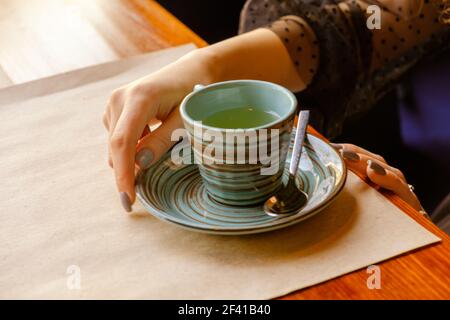 Des couleurs vintage dans la photo des mains et une tasse de thé qui se tient sur la table devant une jeune fille qui tient le bol avec sa main. Des couleurs vintage dans la photo de main et des tasses de thé sur la table Banque D'Images