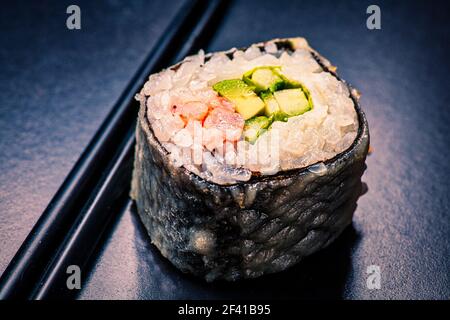 Prise de vue en rouleau de sushi sur fond noir avec reflets, tons d'image dans une couleur vintage. Macro de sushi servi sur fond noir avec réflexion avec baguettes. Macro sushi servi sur noir avec reflet Banque D'Images