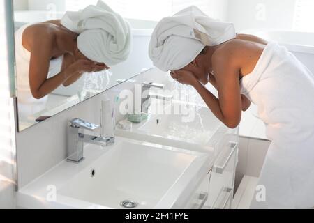 Femme afro-américaine lavant son masque dans le lavabo dans la salle de bains Banque D'Images