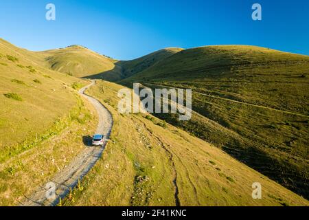 Vue aérienne arrière d'une voiture de sport qui remonte une montagne route sur une colline herbeuse Banque D'Images