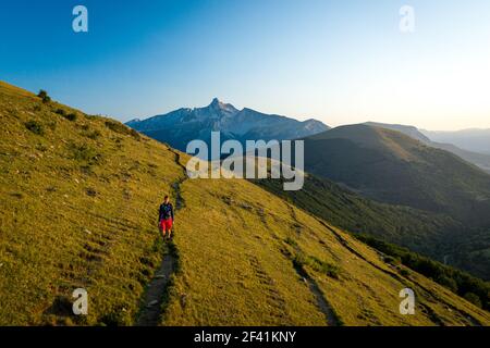 Vue de face d'une personne qui fait de la randonnée sur un sentier de montagne à travers les collines herbeuses Banque D'Images