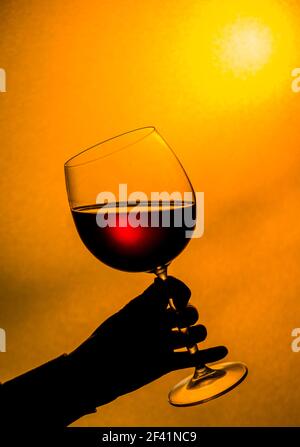 Boire le vin rouge au coucher du soleil. Femme main tenant un verre de vin rouge. Banque D'Images