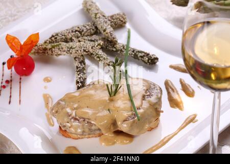 Plat avec mousse de foie gras et asperges au sésame. Gros plan sur une assiette et un verre de vin. Banque D'Images