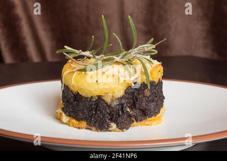 Gros plan d'un gâteau de pommes de terre au beurre avec crème de pudding noire au chocolat, fromage râpé et une branche fraîche de romarin sur une table en bois. Banque D'Images