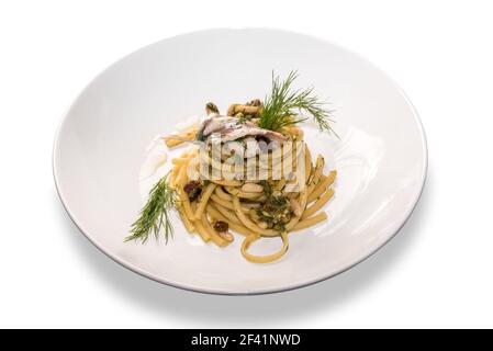 Spaghetti bucatini aux sardines - recette sicilienne avec raisins secs, pignons et fenouil, gros plan dans un plat blanc isolé sur blanc Banque D'Images